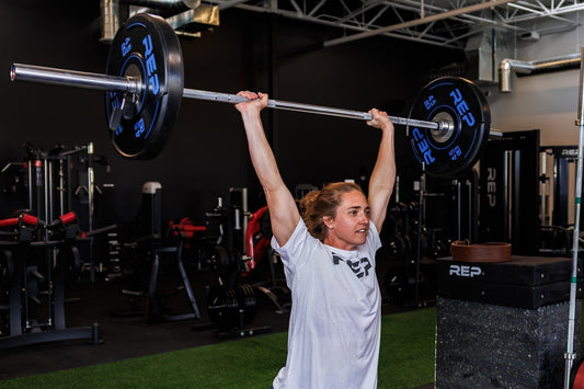Athlete lifts REP barbell and weight plates overhead.