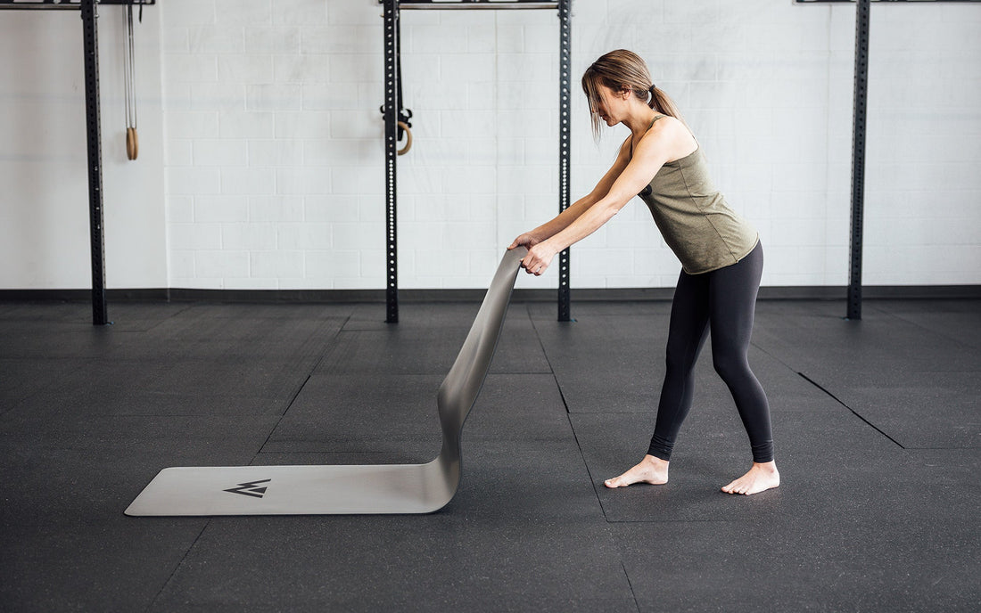 A woman places a yoga mat on the ground, preparing to cool down.